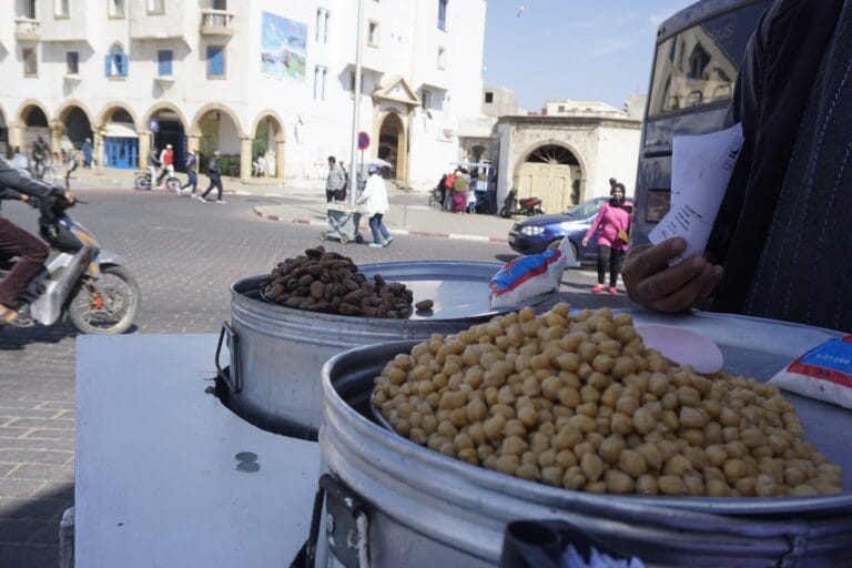 A man stands before a vibrant line of Moroccan street food featuring chickpeas and other local delicacies.
