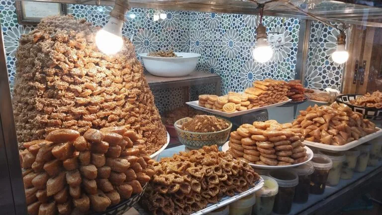Une vitrine présentant un assortiment de sucreries et de pâtisseries marocaines, mettant en valeur leurs couleurs vives et leurs motifs complexes.