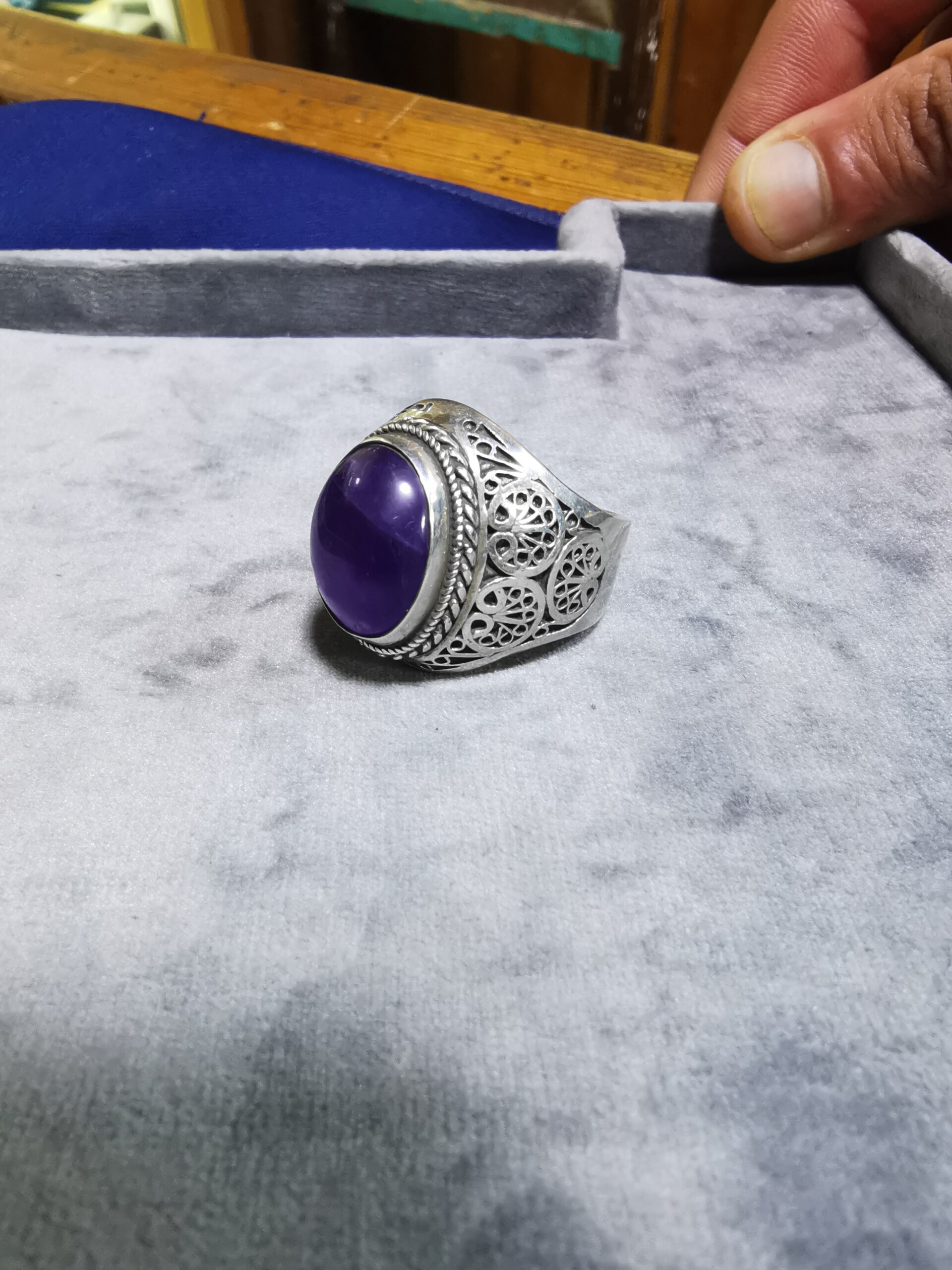 Une magnifique bague en pierre violette repose sur un plateau en argent, mettant en valeur l'orfèvrerie complexe et les influences artistiques arabes.