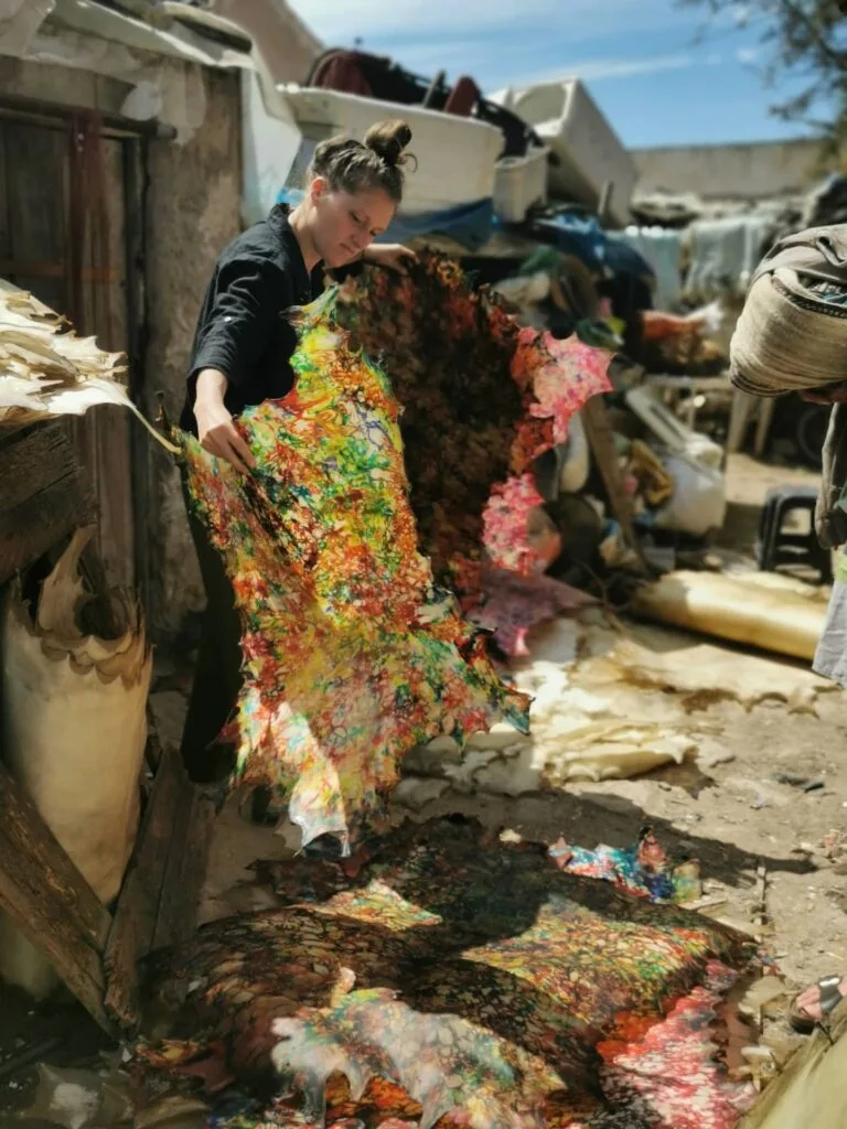 A visitor examining a large, multicolored hand-dyed leather skin during an immersive tour of a local tannery in Essaouira.